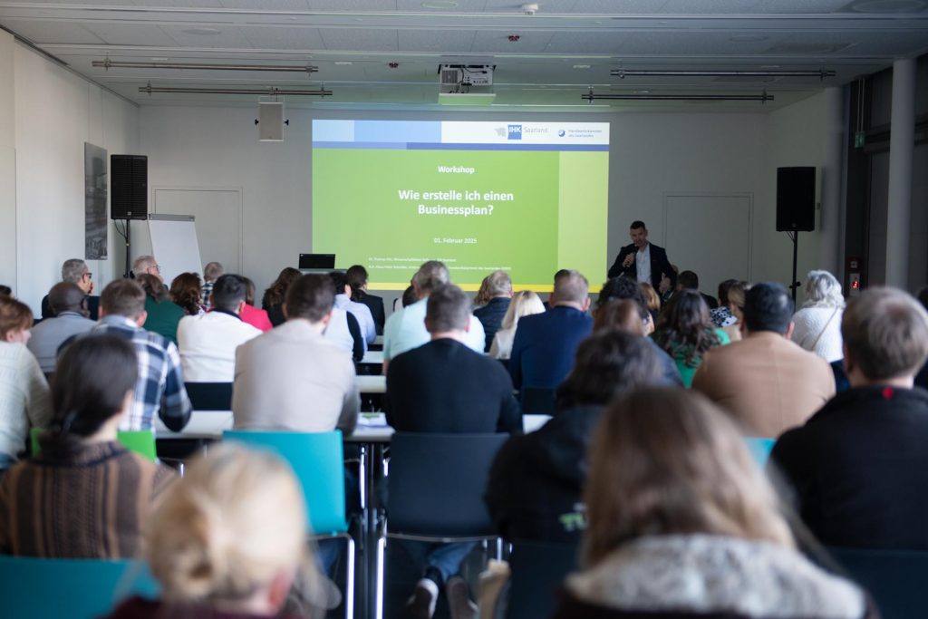 Ein voller Saal von Zuhörerinnen und Zuhörern folgt gespannt einem Vortrag über das Thema der Erstellung eines Businessplans