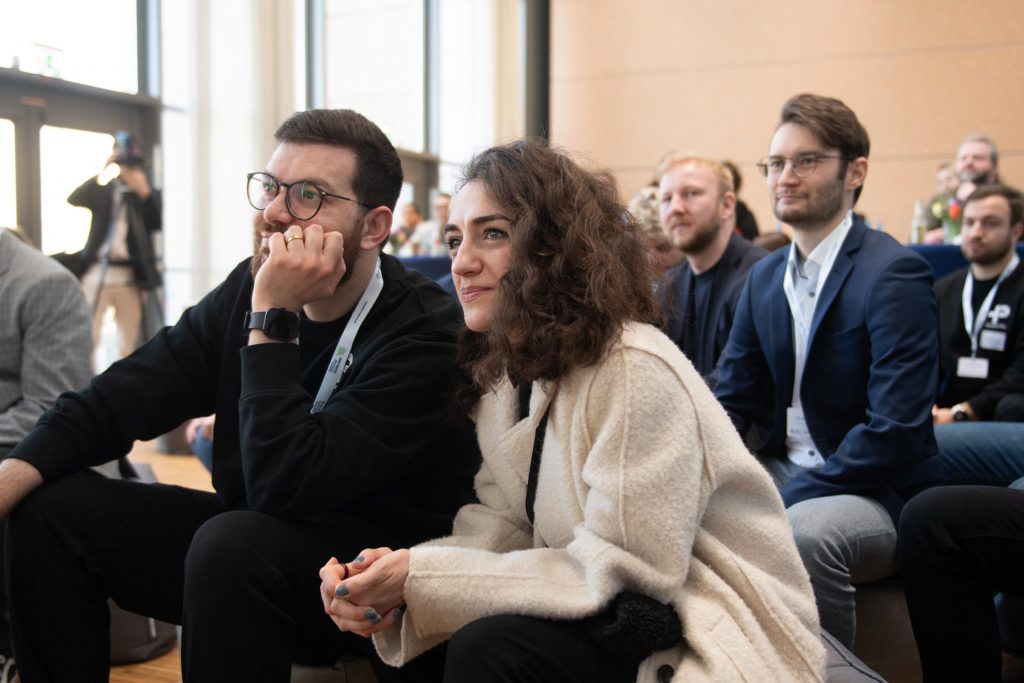 Mehrere Besucherinnen und Besucher der Messe blicken gespannt in Richtung der Bühne