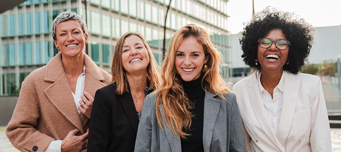 Group of proud businesswomen smiling and looking at camera at workplace. Real executive women staring front, laughing together with suit and successful expression. Corporate female employees meeting. High quality photo