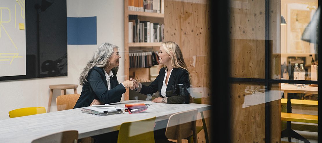 Happy mature and young businesswoman shaking hands in loft office