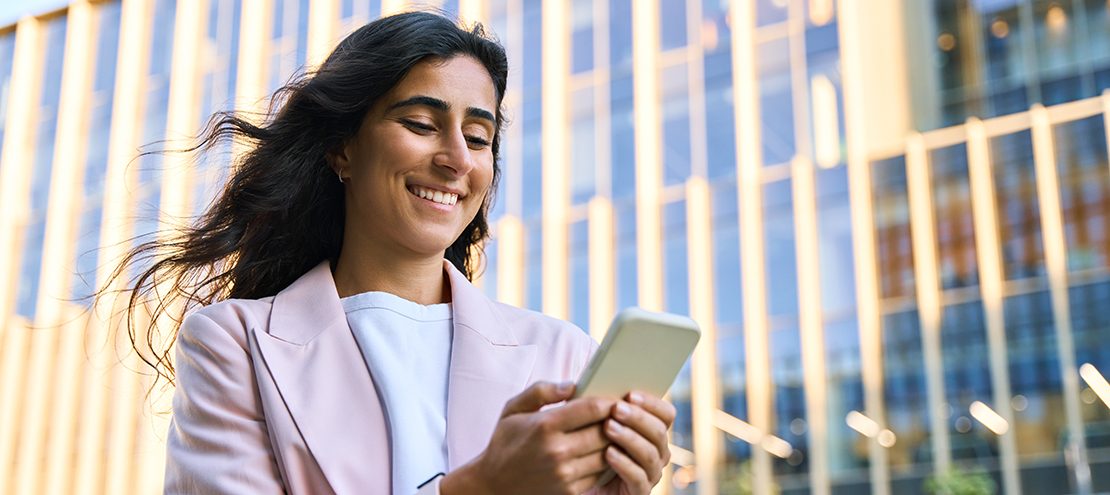 Smiling young middle eastern Israel businesswoman using smartphone mobile phone online app for work at office building. Successful indian or arabic woman in business suit holding cellphone. Copy space